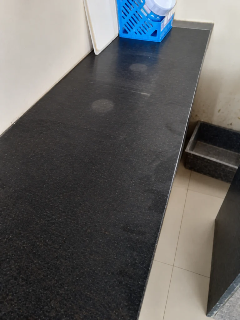 Dark speckled granite counter top fixed along a cream wall, with a basket and chopping board at the far end