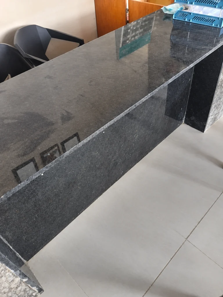 Long polished dark granite counter top with a matching granite front panel, chairs behind it