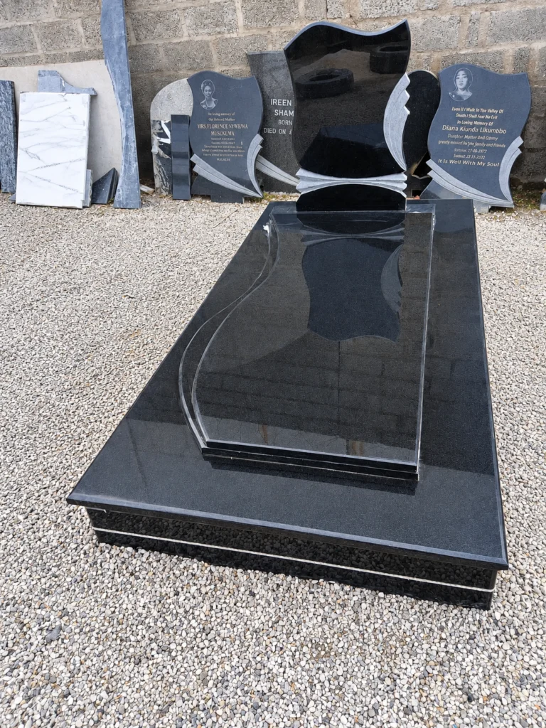Wave-shaped black granite headstone with grey fan details, on a raised ledger with a sculpted inner panel