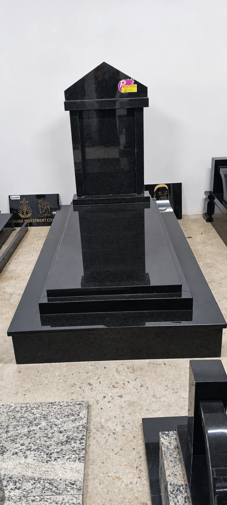 Tall black granite headstone with a pitched top and framed panel, on a stepped ledger