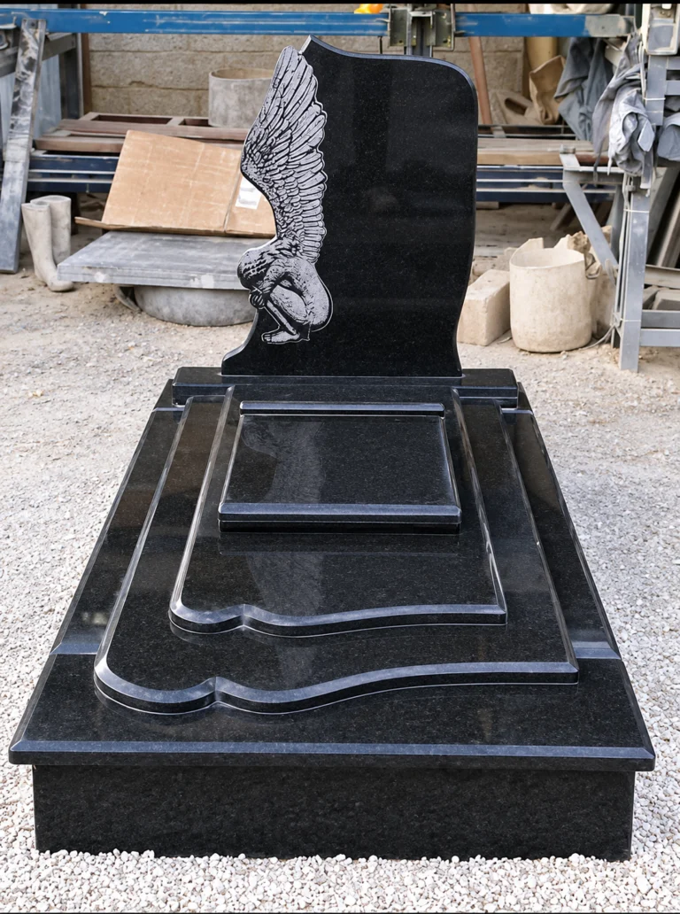 Shaped black granite headstone with a detailed etched angel, above a tiered ledger