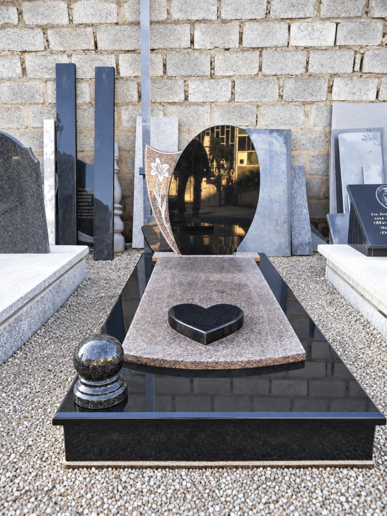Oval black headstone beside an engraved lily panel, with a red granite cover slab, black heart and sphere ornament