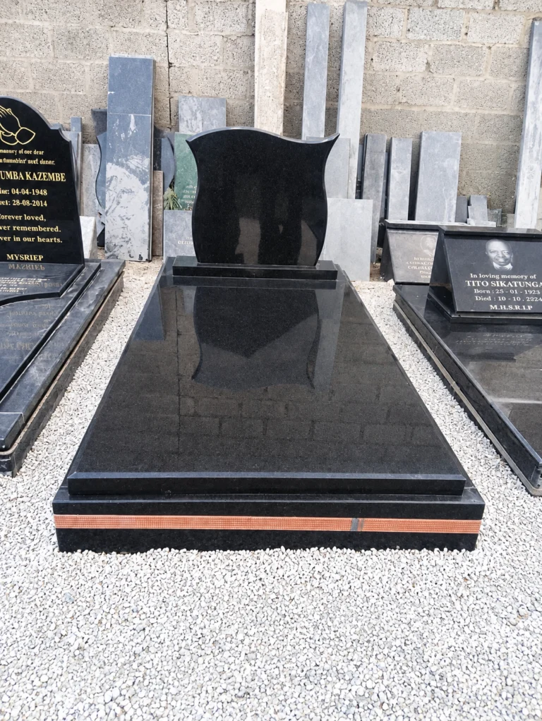 Shaped black granite headstone on a full polished ledger with a copper-coloured band around the base